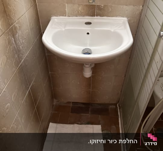 כיור רחצה תלוי מחרסינה וברז סוללה מותקן בקיר חדר הרחצה
